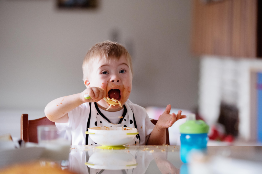 Criança com síndrome de down se alimentando feliz.